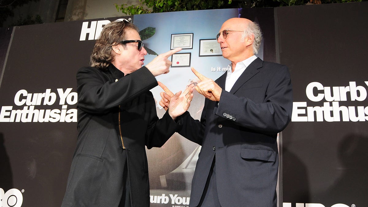 Richard Lewis and Larry David laughing and pointing at each other on the red carpet