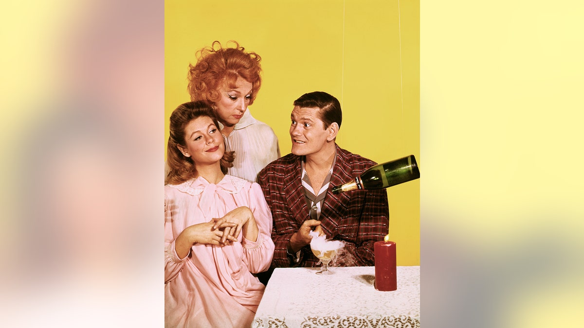 Elizabeth Montgomery, Agnes Moorehead, and Dick York posing next to a table with champagne pouring itself