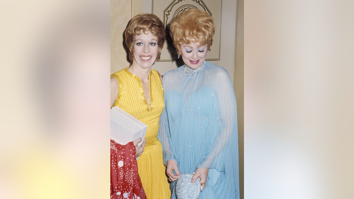 Carol Burnett mengenakan gaun kuning di samping Lucille Ball yang mengenakan gaun biru