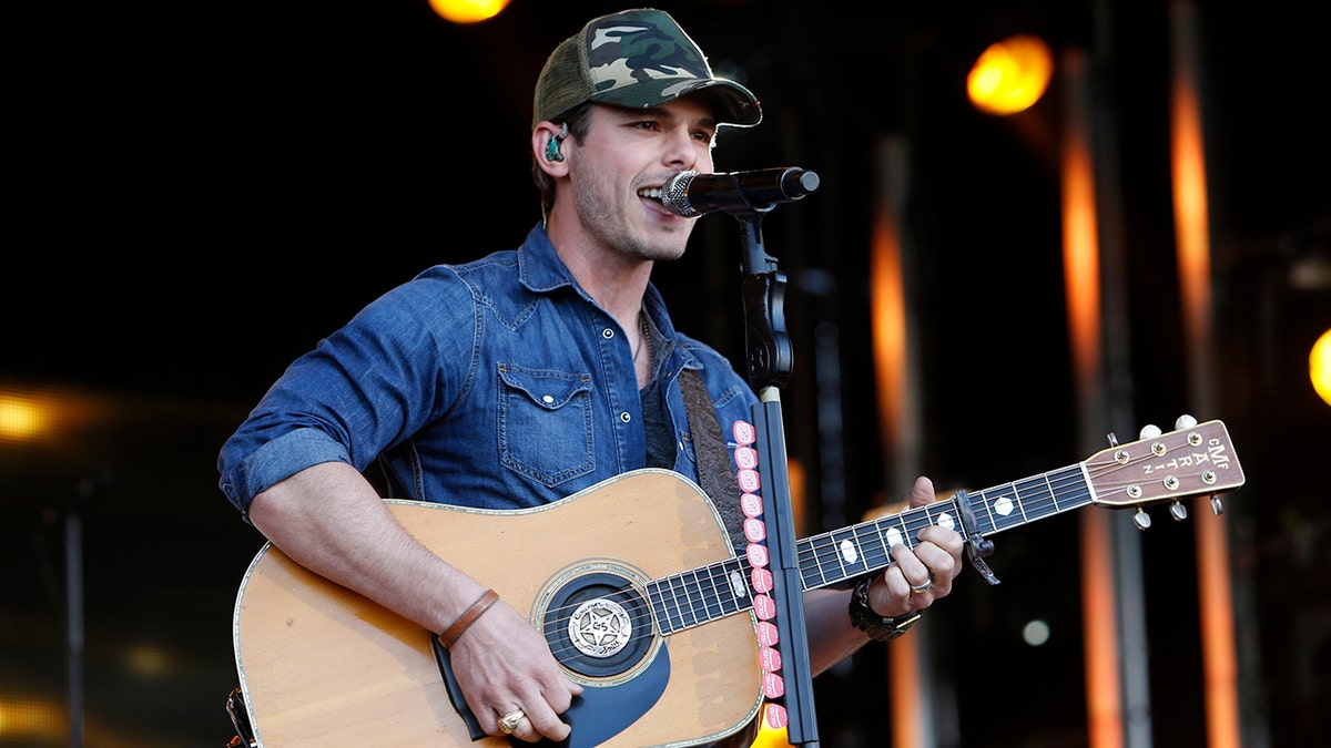 Granger Smith performing on stage wearing a denim shirt while holding a guitar