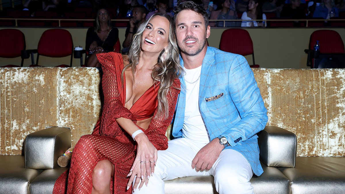 Jena Sims in a red low-cut dress next to Brooks in a white shirt and pants with a bright blue leather jacket
