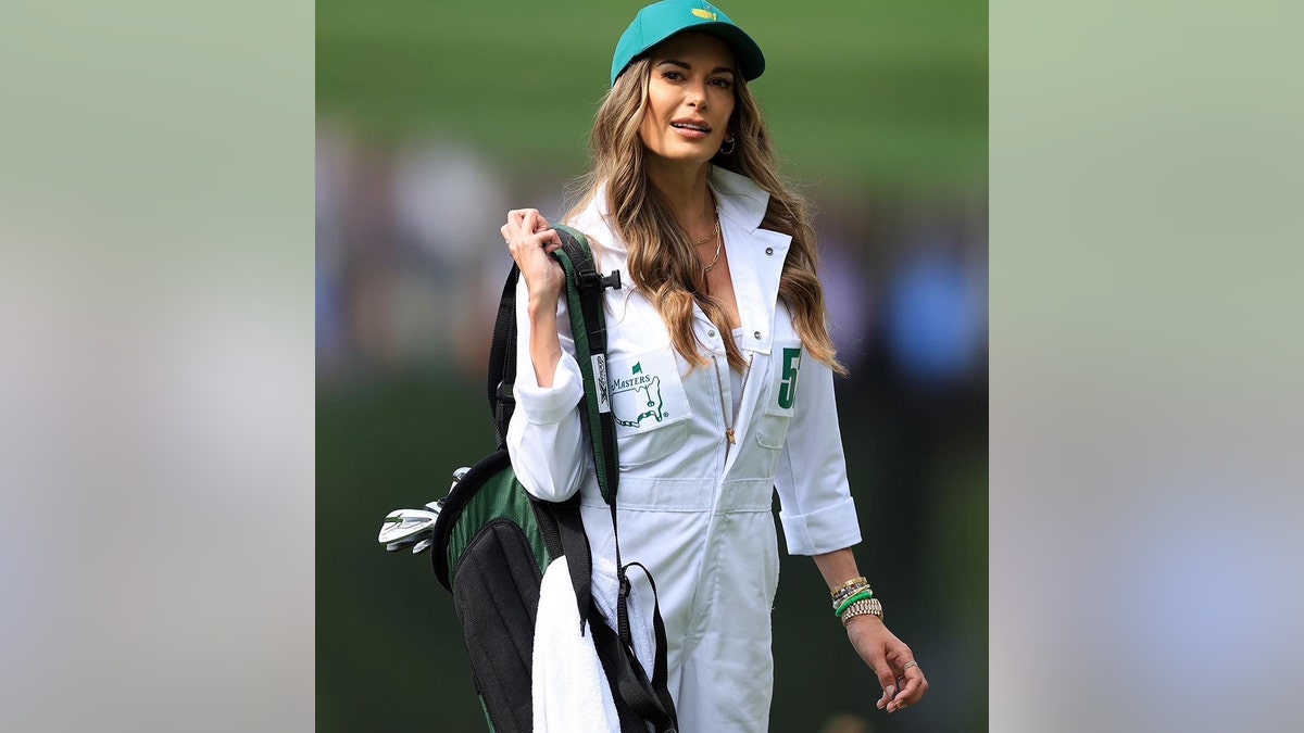 Jena Sims in a white caddy uniform holding golf clubs