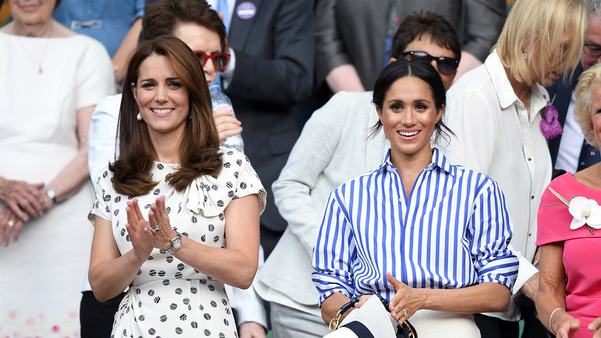 Kate Middleton wearing a white printed dress next to Meghan Markle wearing a blue and white striped blouse holding a wide brimmed hat