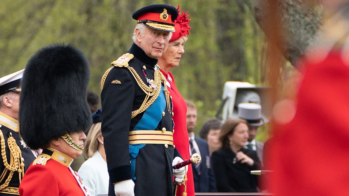 King Charles in a military uniform next to Queen Camilla in a red dress with a matching hat