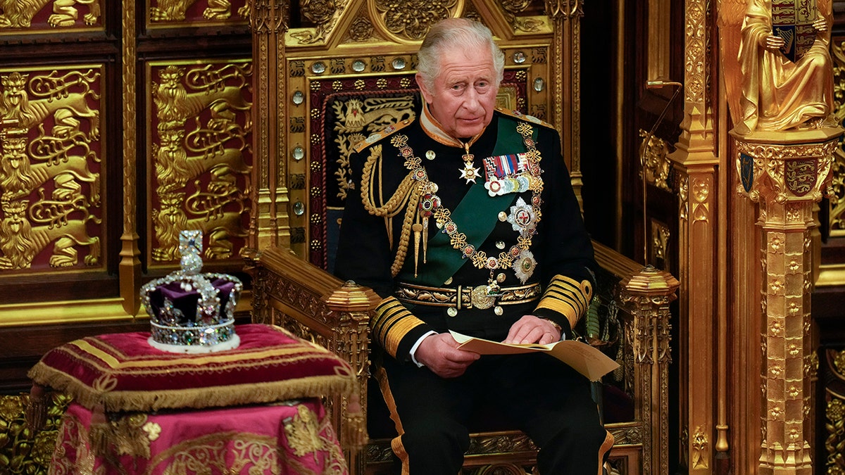 King Charles in royal regalia sitting on a throne next to a crown