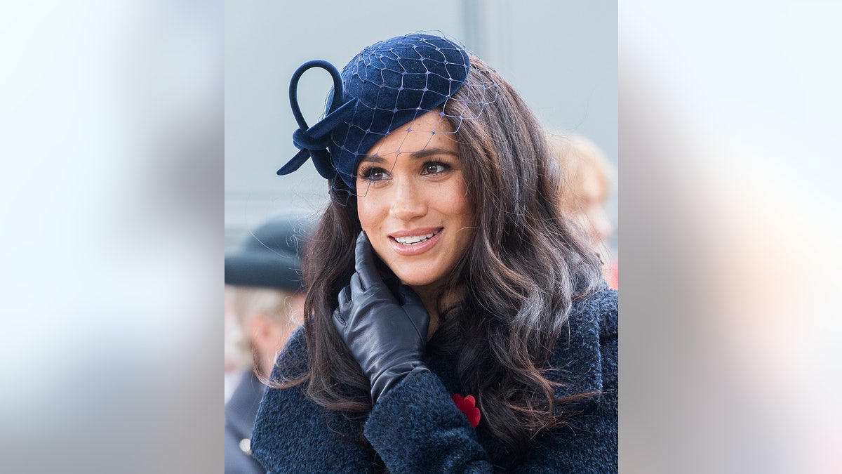A close-up of Meghan Markle in a dark coat dress with a matching fascinator