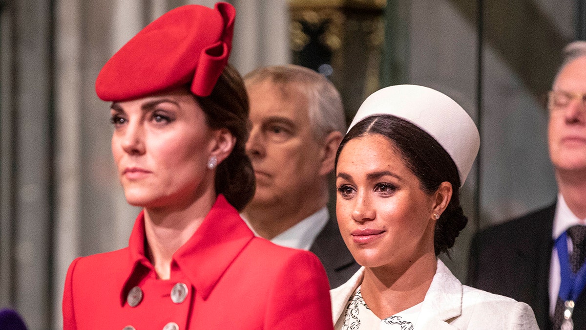 A close-up of Kate Middleton in a red dress and a matching hat next to Meghan Markle in a white dress with a matching hat
