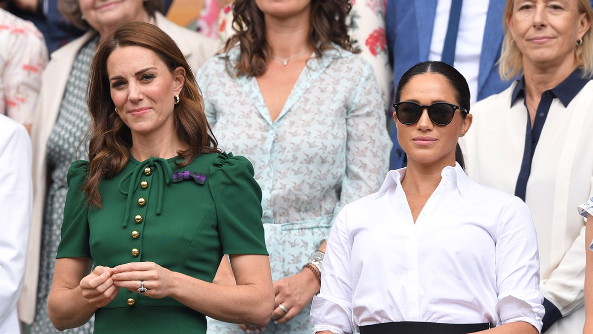 Kate Middleton wearing a green dress next to Meghan Markle wearing a white blouse and sunglasses