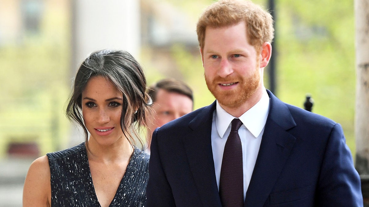 Meghan Markle wearing a black sparkling dress next to Prince Harry in a suit and tie