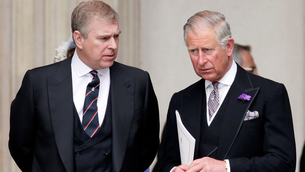 Prince Andrew and King Charles wearing suits and ties looking sternly at each other