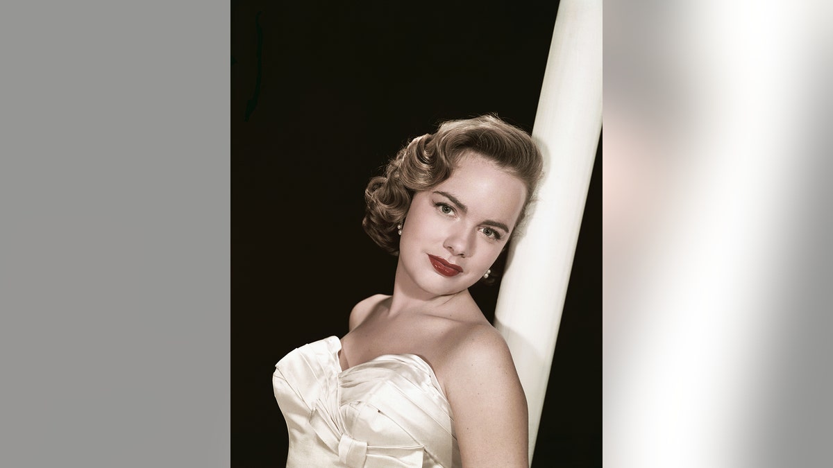 Terry Moore in an ivory strapless dress leaning against a white pole