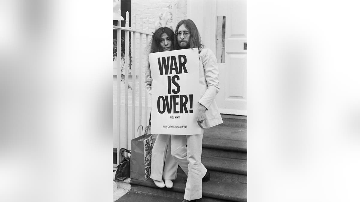 John Lennon and Yoko Ono wearing white holdiing a war is over sign
