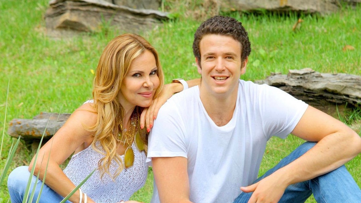 Ana Obergón in a white tank-top and jeans leans on her son Aless in a white t-shirt and jeans sitting on the grass 