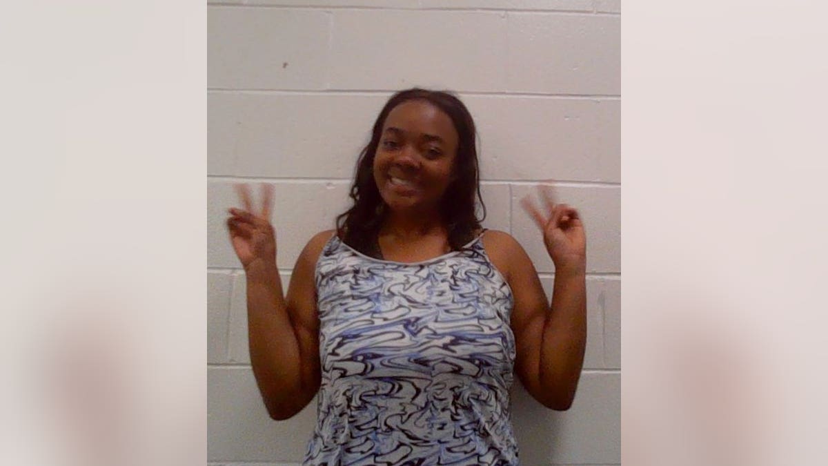 Kayiba K. Christelle smiles and flashes peach signs in mugshot