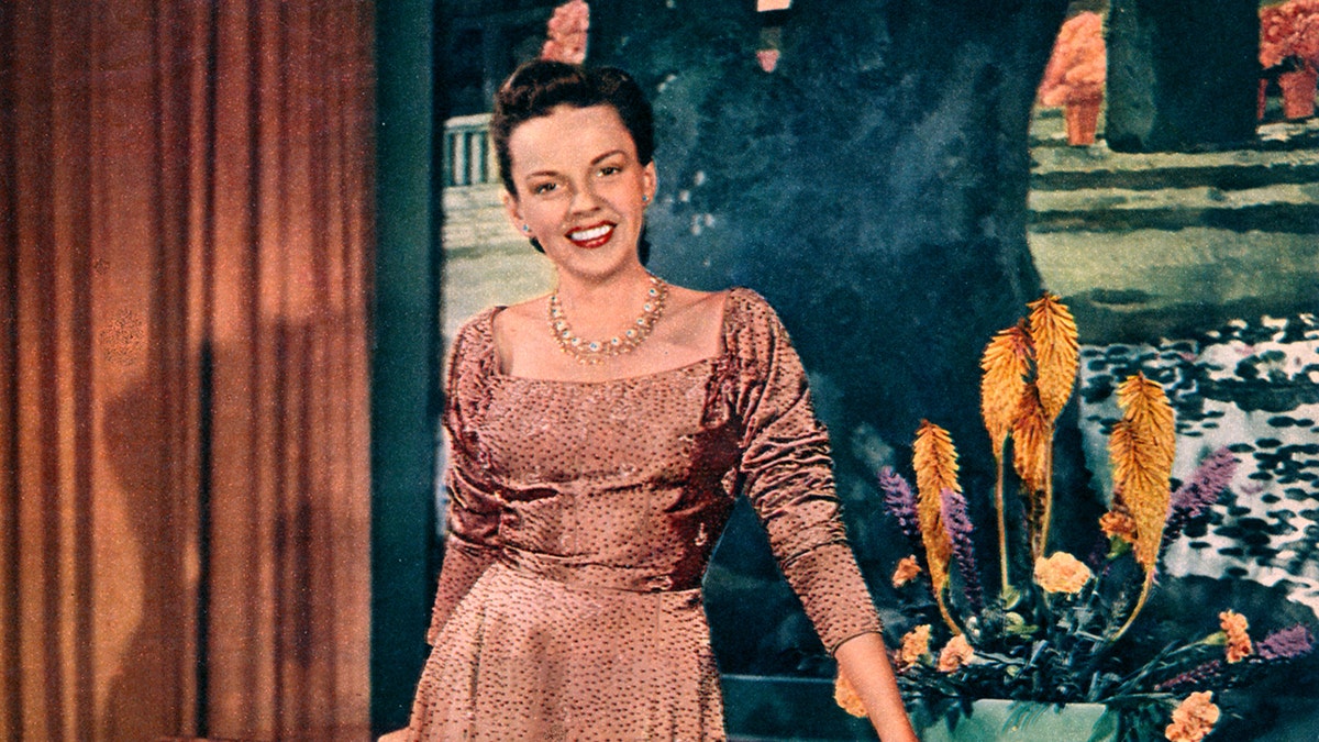 Judy Garland smiling wearing a pink dress.