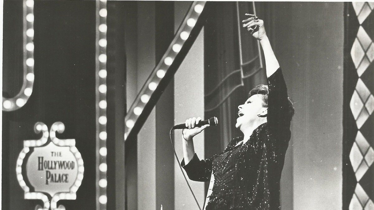 Judyy Garland singing on stage raising her hand