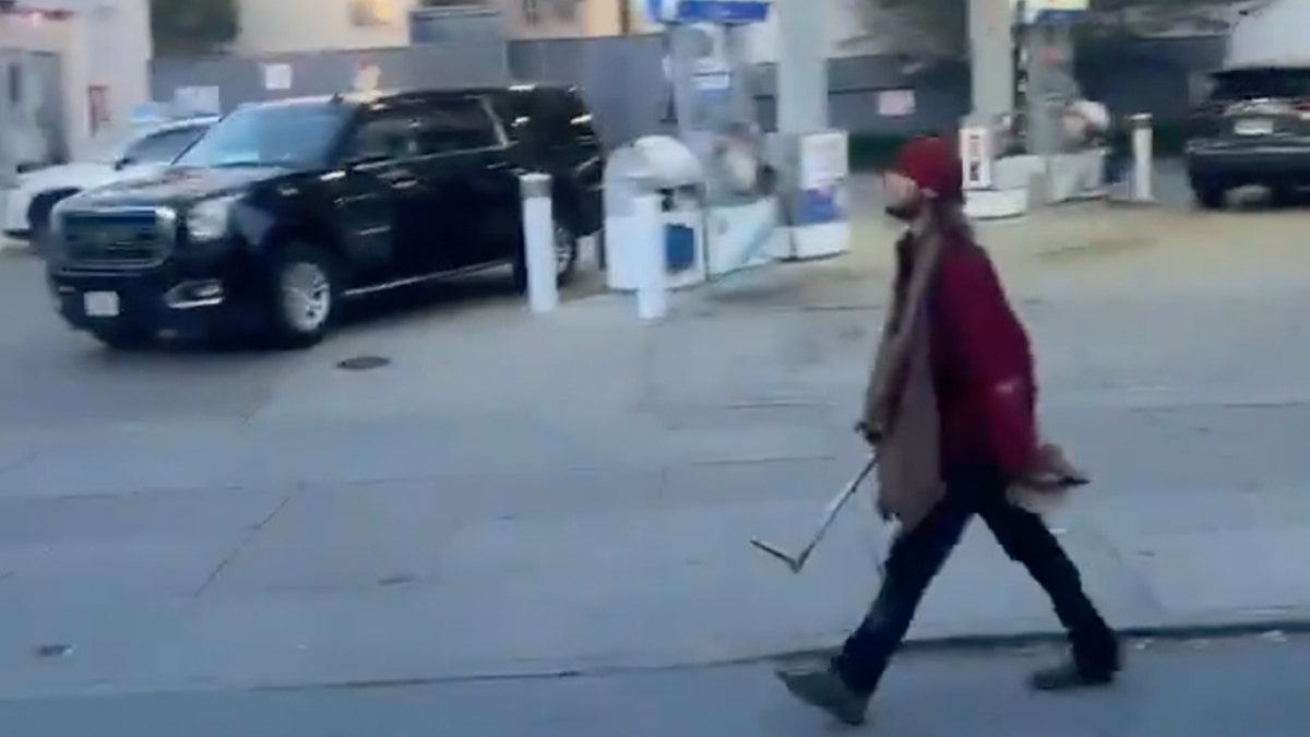 Man in ragged clothes carrying pipe down street