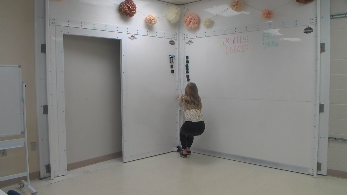 A teacher pulls the handle of the collapsed bulletproof shelter to show how it sets up