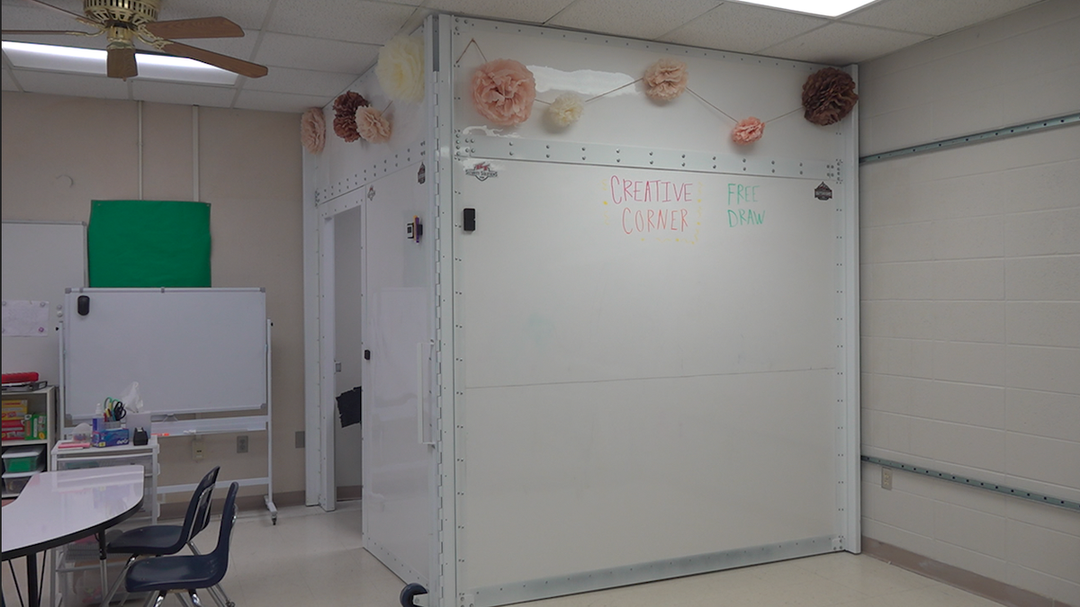 An 8-by-8 foot room stands in the corner of a classroom. On the outside is dry erase material with classroom decorations on it