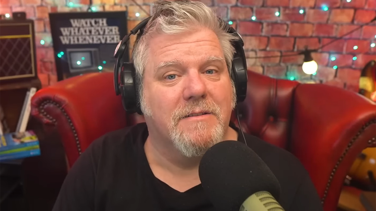 Craig Duncan in a black shirt sarcastically speaks into a microphone wearing black headphones talking about his time with James Corden