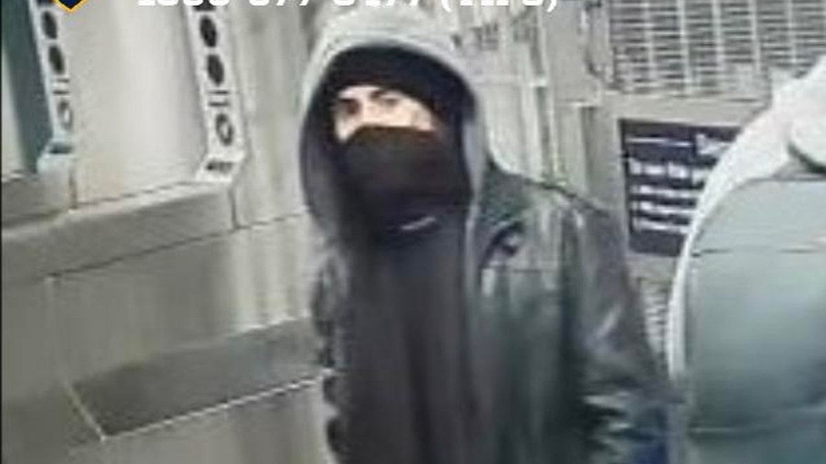 Man in black mask and gray hood walks through subway turnstile