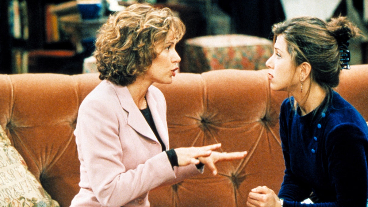 Jennifer Grey in a pink blazer stars as Mindy Hunter and talks with her hands out to Jennifer Aniston as Rachel Green on an episode of "Friends" sitting on the orange couch