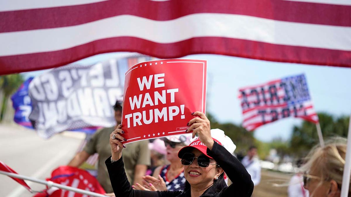Supporters of former President Donald Trump hold signs and wave flags in support of Trump outside Trump International Golf Club