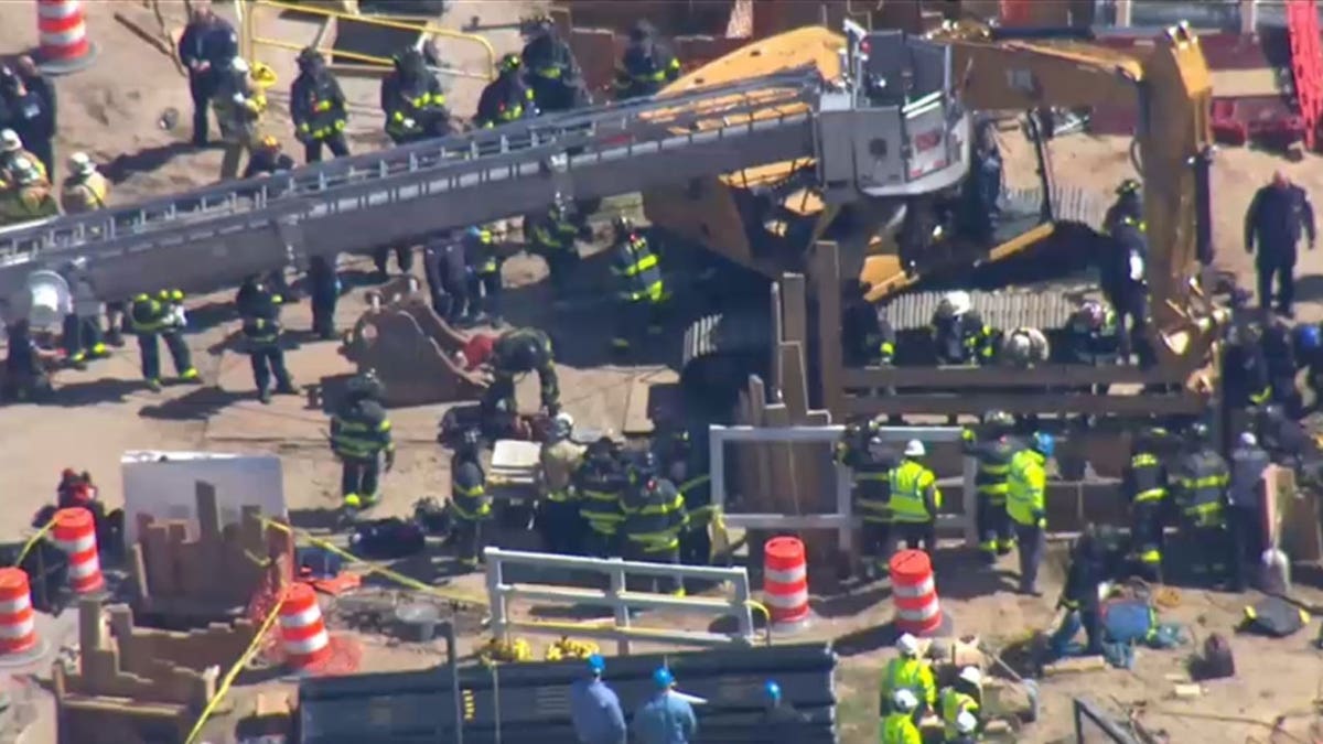 New York Fire Fighters surrounding a trench with a crane and a construction vehicle.