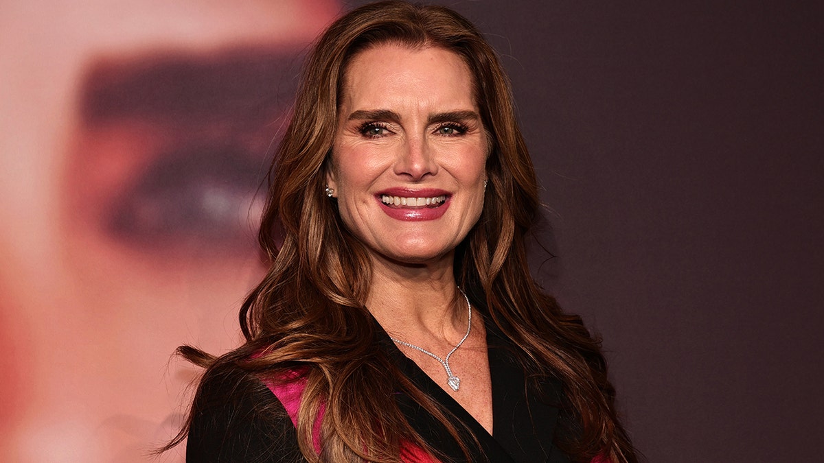 Brooke Shields smiles in a black jacket with a pink sash