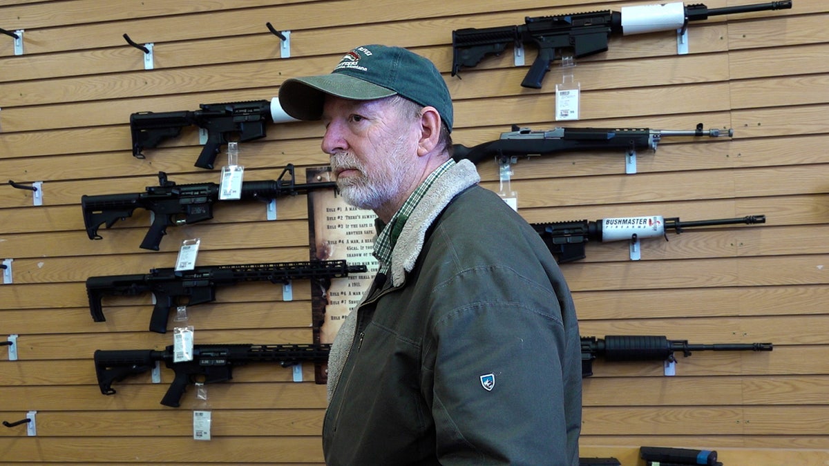 Gun store manager Bruce Smith stands in front of semiautomatic rifles hanging on the wall