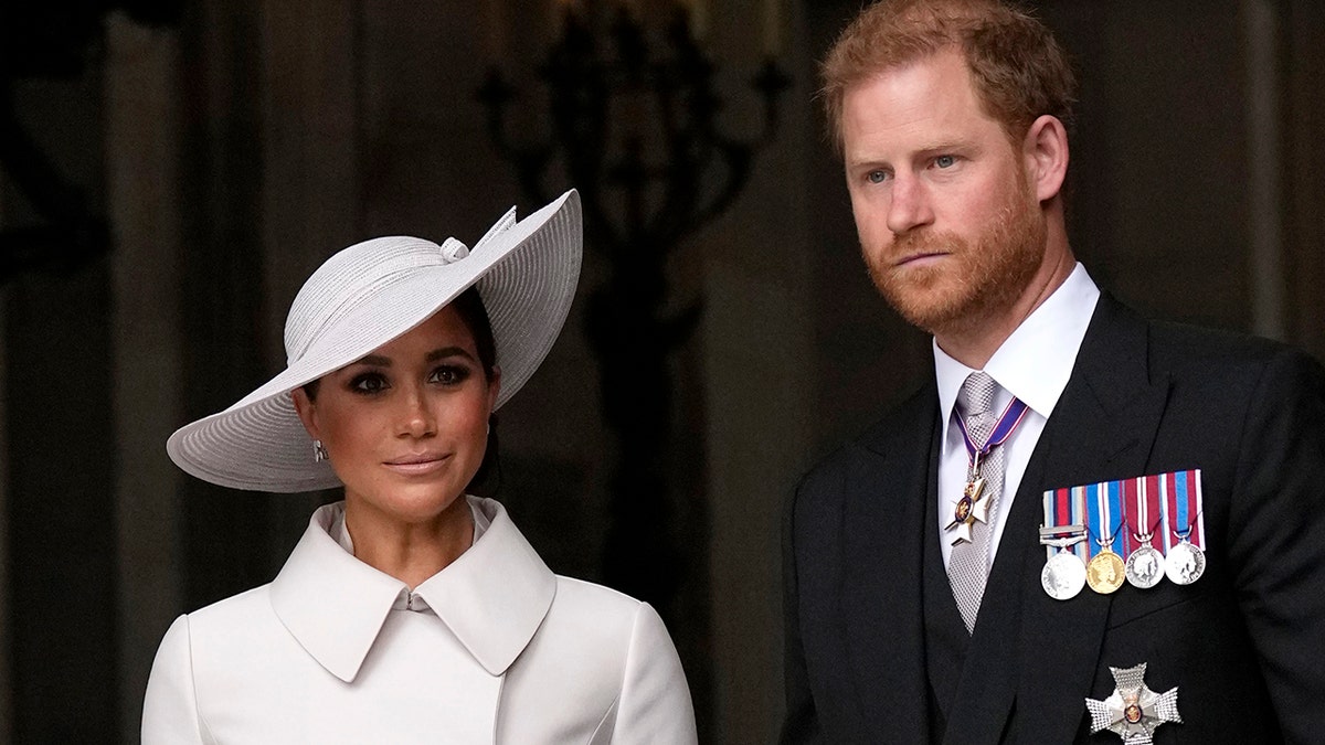 Meghan Markle in a white coat dress and a matching white hat with Prince Harry in a suit and tie