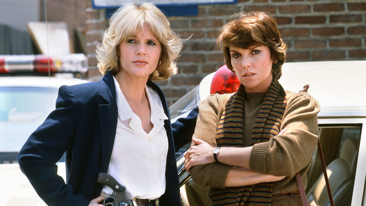 Cagney and Lacey stars Sharon Gless and Tyne Daly stand in front of police cruiser.