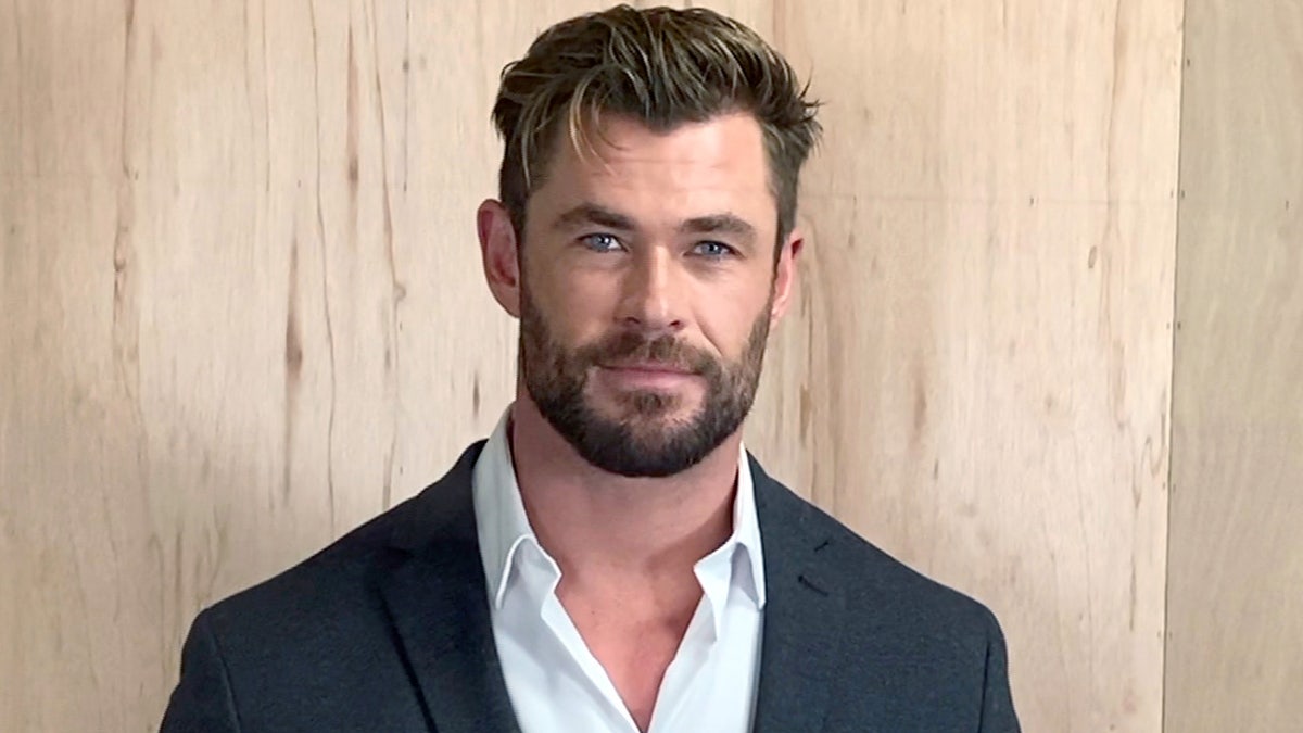Chris Hemsworth poses for image convention wearing suit overgarment and button-down shirt