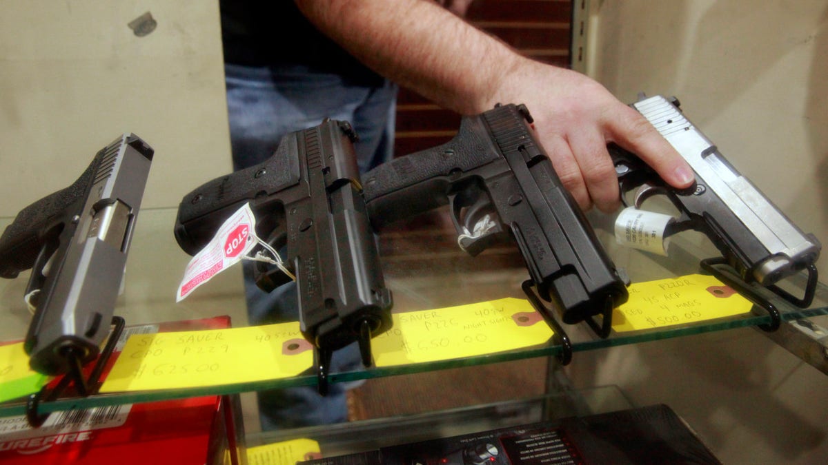 man holding gun that's in display case with other guns