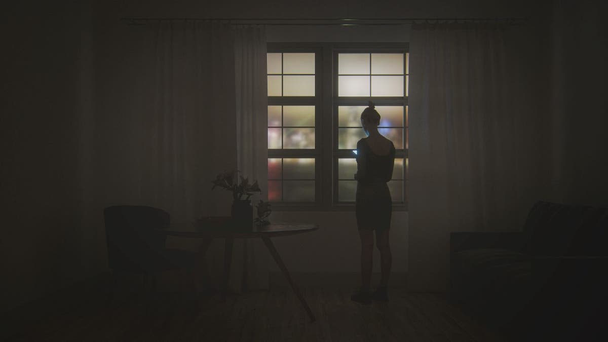 Woman stands near window in dark room