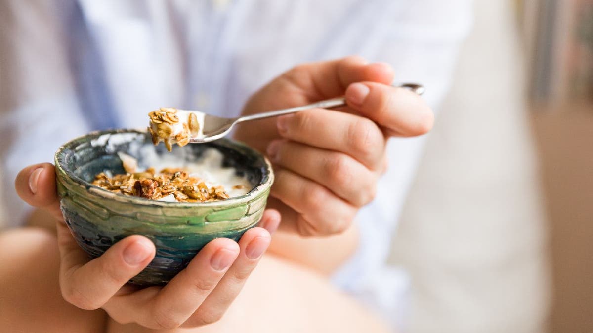 Person eats parfait-like dish with granola