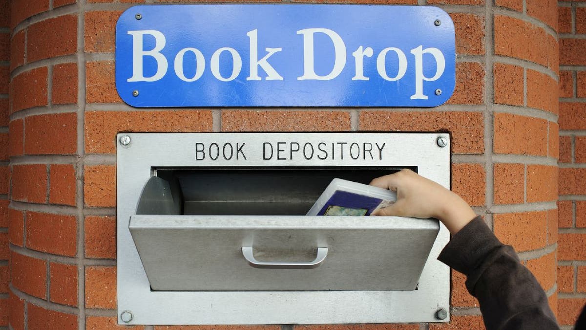 A hand return a borrowed item at library book drop box.