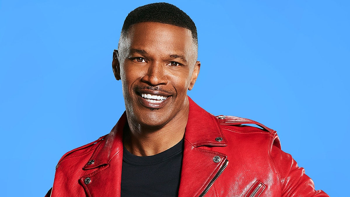 Jamie Foxx wears red jacket and black shirt while smiling for portrait shot