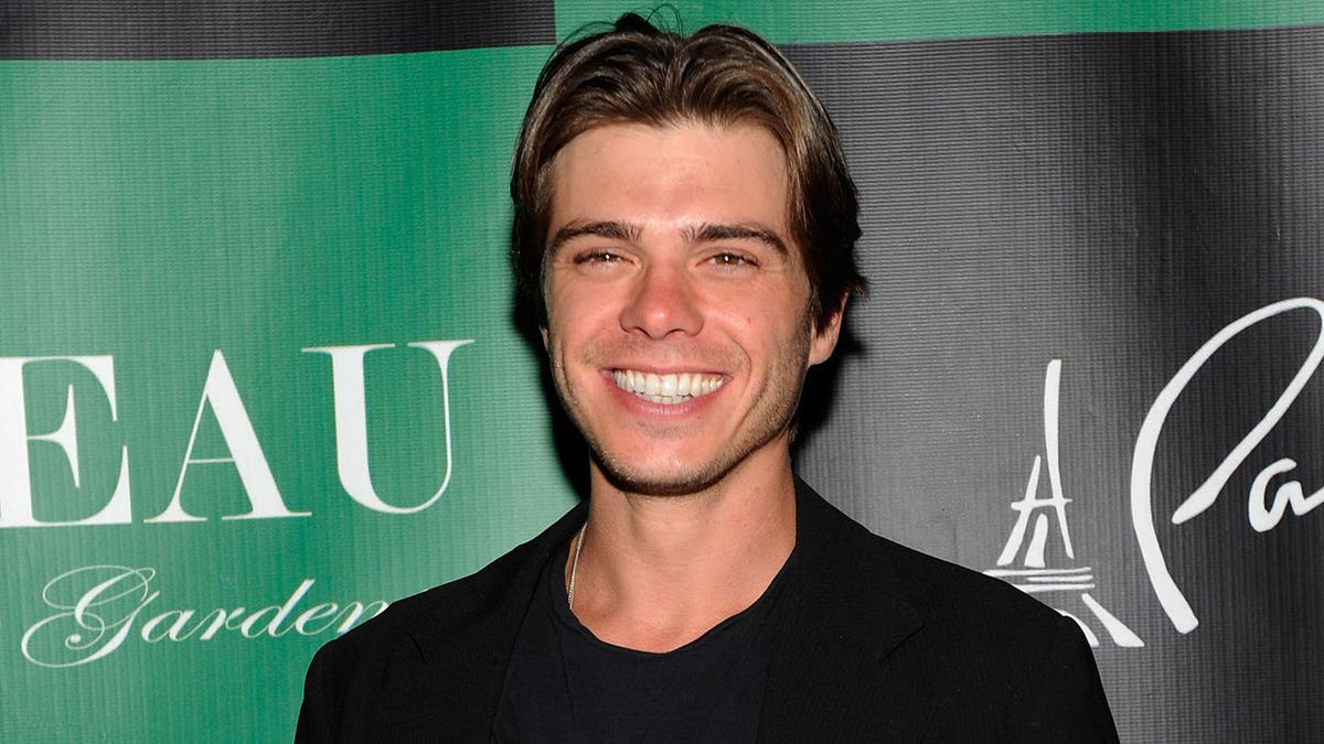Matthew Lawrence wears black outfit in front of a green background