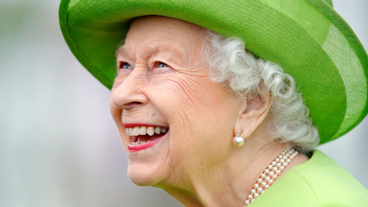 Queen Elizabeth gives a big smile while wearing a bright green coat with a matching hat.