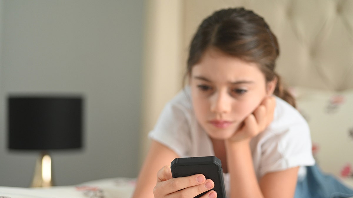 young girl looks at cell phone on bed