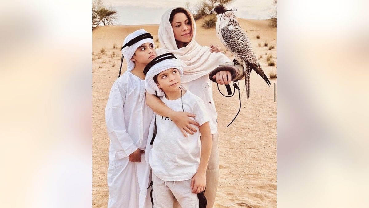 Shakira and her sons Milan and Sasha, all wearing white and head covers in the desert, as a bird lands on Shakira's arm