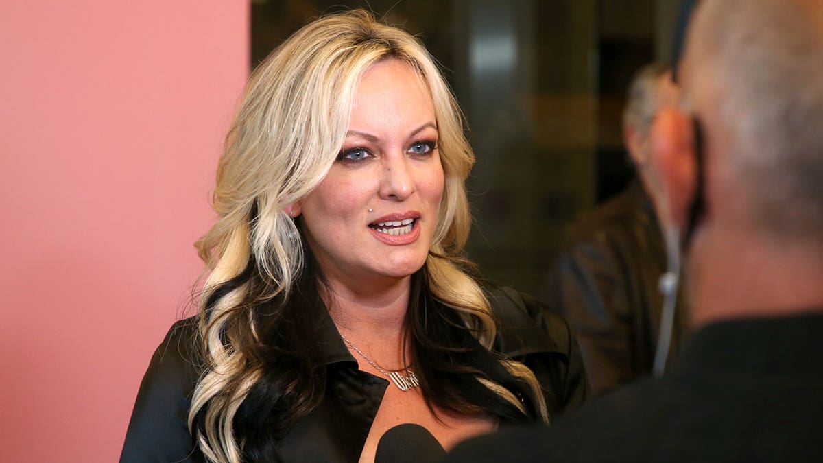 Stormy Daniels stands in front of a pink background