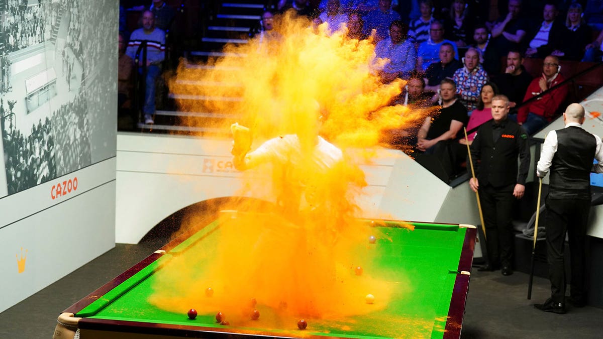 A 'Just Stop Oil' protester jumps on the table and throws orange powder during a World Snooker Championship match in Britain on April 17, 2023.?