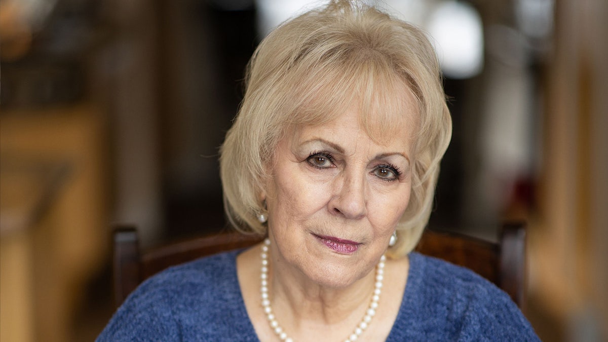 Cancer survivor Vicki Baker looks at the camera, wearing a blue shirt, earrings, and a pearl necklace