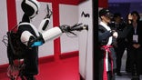 An operator, right, controls a 5G humanoid robot as it paints on the NTT DOCOMO Inc. stand during the opening day of the Mobile World Congress (MWC) in Barcelona, Spain, on Monday, Feb. 26, 2018. At the wireless industry's biggest conference, more than 100,000 people are set to see the latest smartphones, artificial intelligence devices and autonomous drones exhibited by roughly 2,300 companies. Photographer: Angel Garcia/Bloomberg via Getty Images