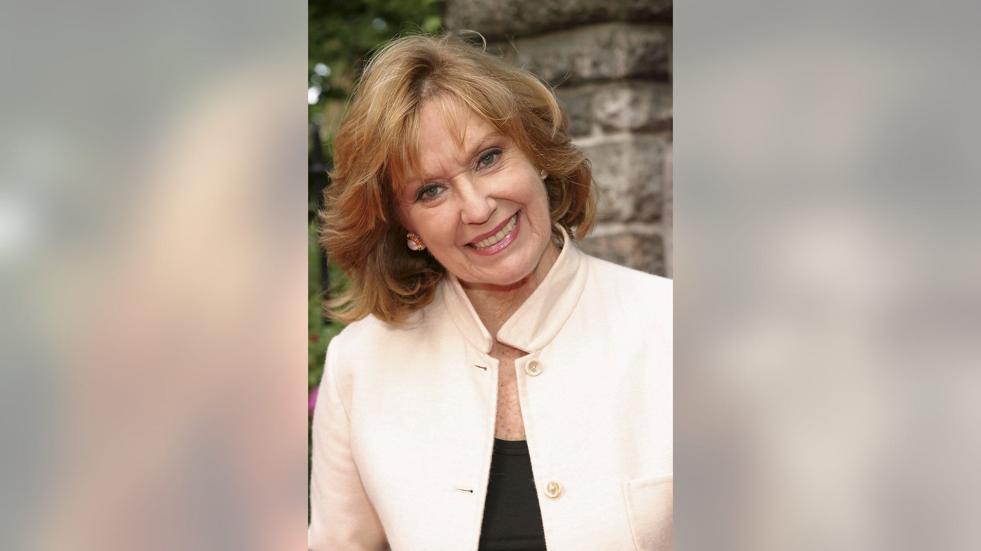 Elizabeth Hubbard smiling with head tilted in cream jacket