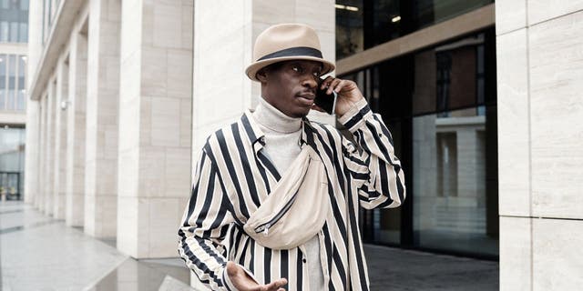 Man dressed in a white-and-black striped suit putting his phone to his ear