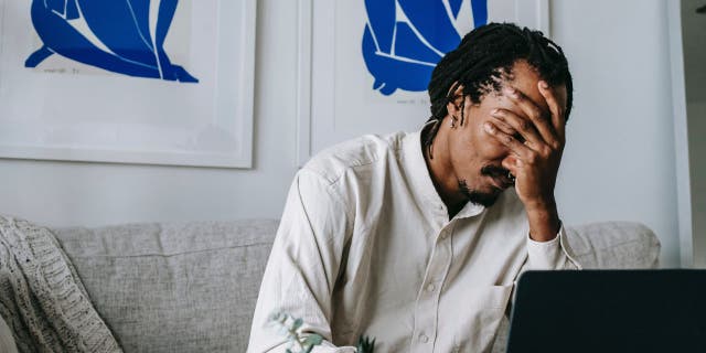 Man sitting on the couch with his hand over his face.