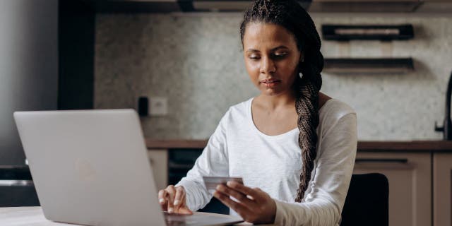 Wanita memegang kartu kredit dan mengetik di laptopnya.